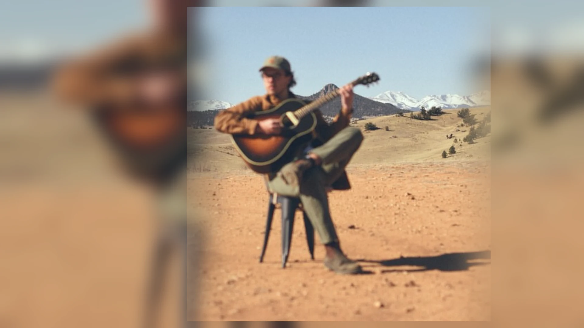 Quincy Landers seated with an acoustic guitar in the Colorado landscape