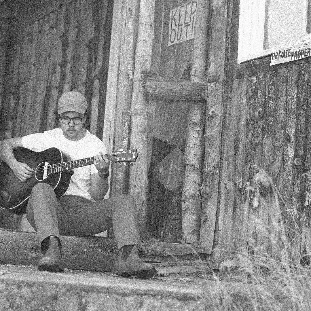 Quincy playing acoustic guitar outside an old wooden building