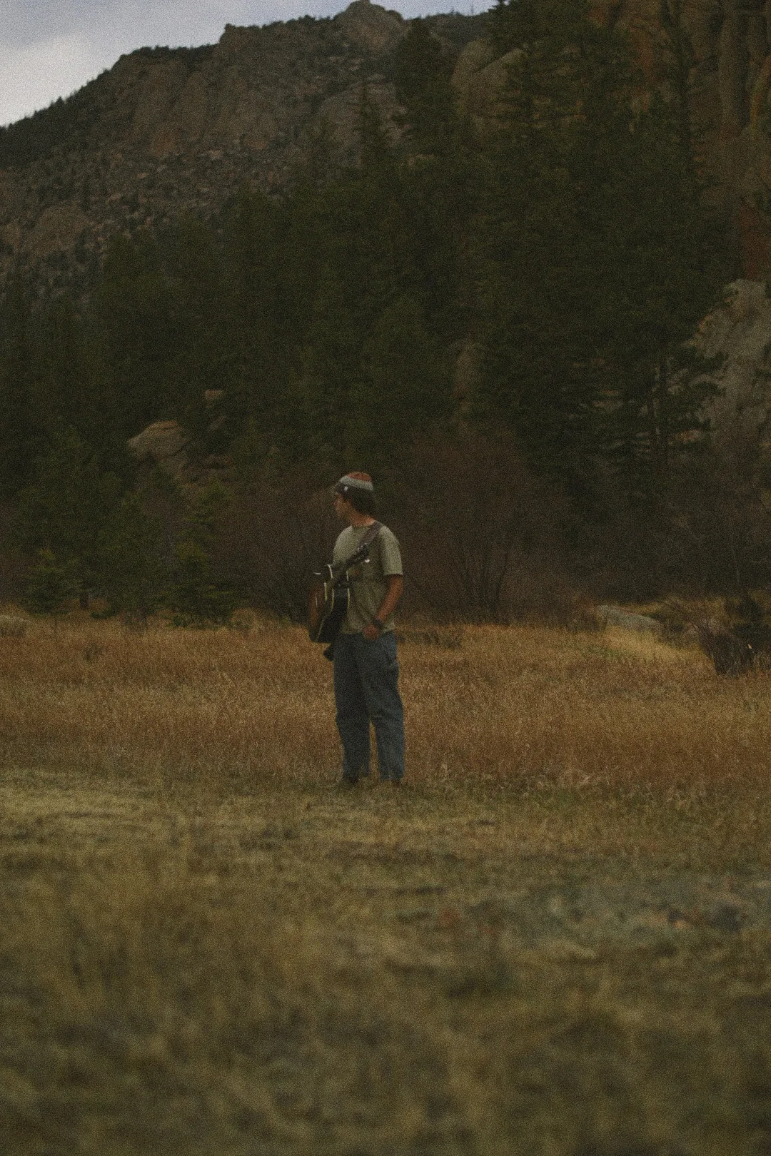 Quincy standing with his guitar in a Colorado meadow